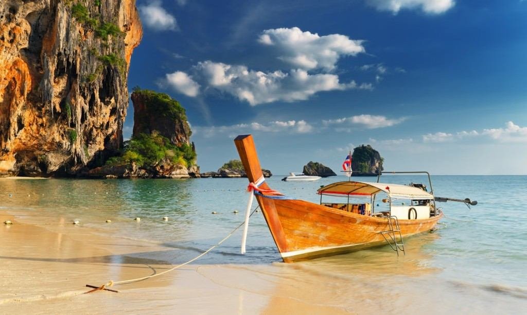 Traditional long-tail boat on turquoise water beside limestone cliffs in Thailand